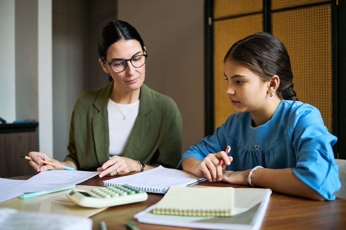A tutor working one-on-one with a school-age student on math homework at a desk